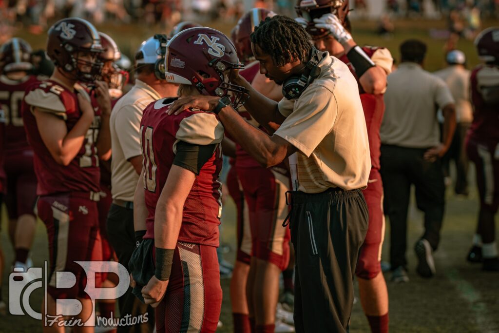 a coach on the football field looking directly into his student's eyes